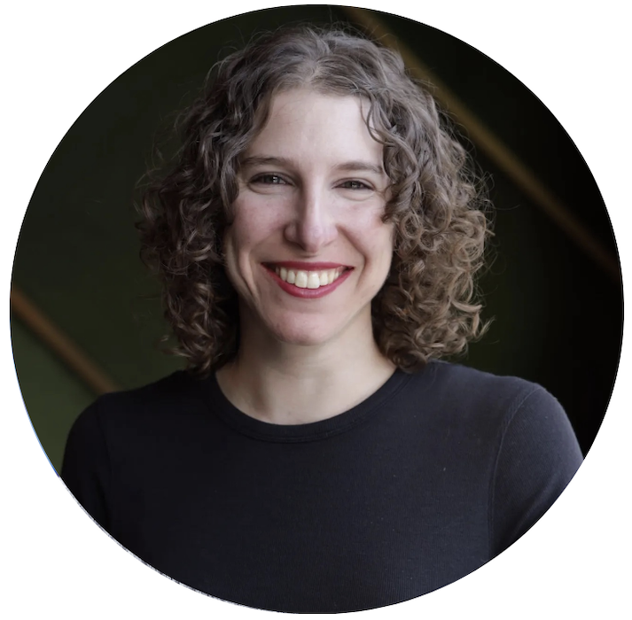 Sabrina grins, her face is well lit and contrasts with her black shirt and dark background