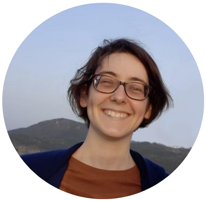 Patrícia grins joyfully, dressed in casual clothes. Behind her, we see mountains under a clear sky.