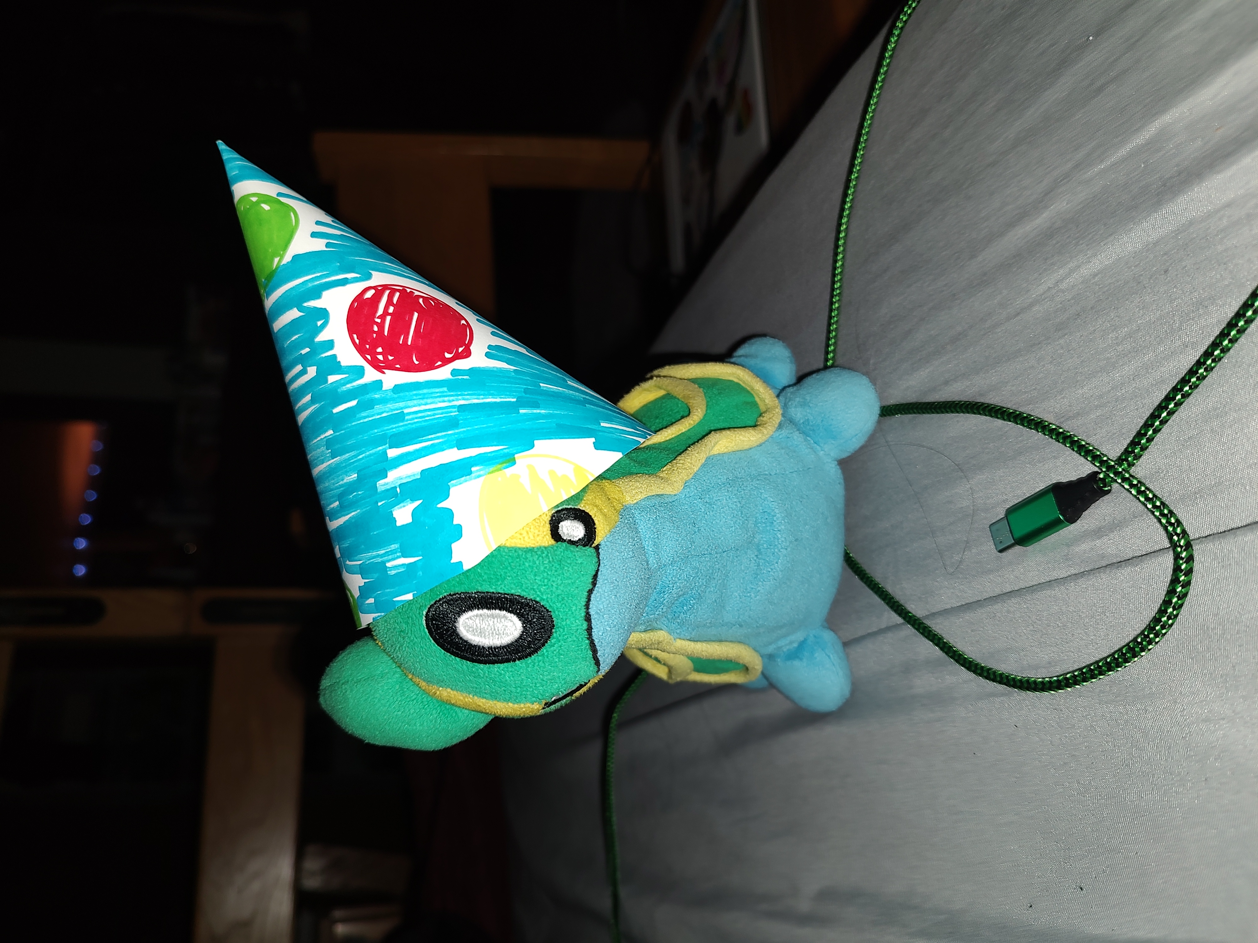 A picture of an east sea gastrodon plush in a dark room wearing a party hat too big for its head