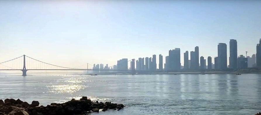 View of skyscrapers and a distant suspension bridge on the other side of the wide Yangtze River, under a clear sky with sunlight. View of skyscrapers and a distant suspension bridge on the other side of the wide Yangtze River, under a clear sky with sunlight.