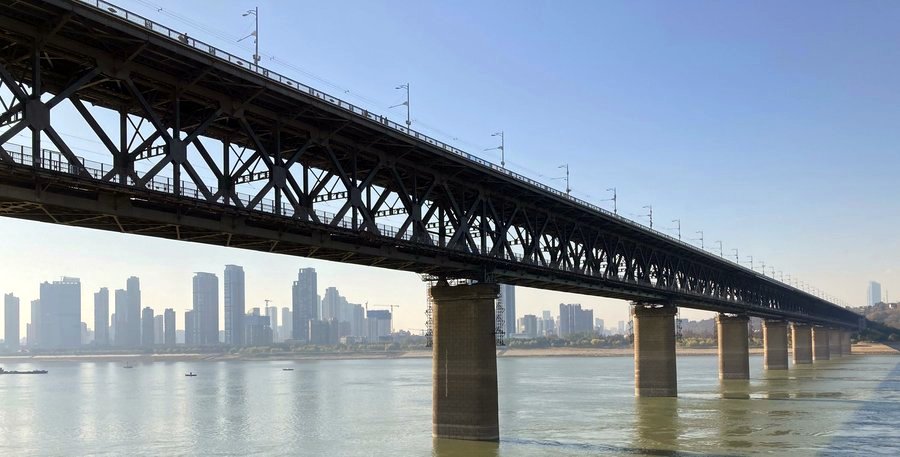 The Wuhan Yangtze River Bridge looming above the water, with skyscrapers behind the bridge.